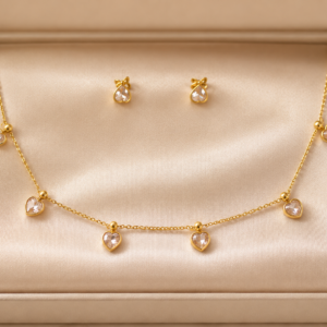 Woman wearing a gold-toned heart drop charm necklace with matching crystal heart stud earrings.
